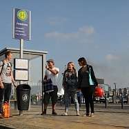 Symbolfoto. Fröhliche Personen stehen an einer Bushaltestelle.