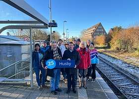 Burkhard Gerling u Jochen Schulz mit Schild am Bahnhof, Aufschrift 25 Jahre Husby