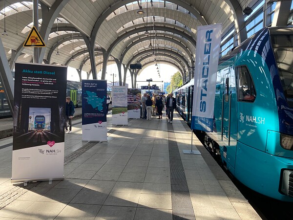 Gleis 6 im Kieler Hauptbahnhof mit Akkuzug und Roll-Ups und Besucher*innen