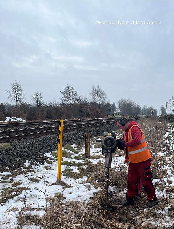 Ein Mann steht neben der Schiene und arbeitet sich mit einem Handbohrer durch den Boden.