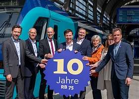 Gruppe vor Zug mit 10 Jahre RB 75 Schild