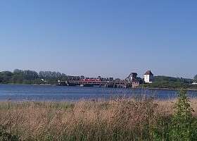 Foto von der Schleibrücke in Lindaunis, über die ein roter Zug fährt.