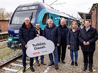 © nordbahn/ Axel Heimken Menschengruppe vor Zug mit Tschüss, Diesel Schild