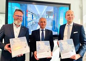 Verkehrsminister Claus Ruhe Madsen, Müslüm Yakisan von Alstom und Dr. Arne Beck von NAH.SH zeigen Vertragsordner über Elektrotriebzüge für Schleswig-Holstein