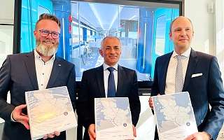 Verkehrsminister Claus Ruhe Madsen, Müslüm Yakisan von Alstom und Dr. Arne Beck von NAH.SH zeigen Vertragsordner über Elektrotriebzüge für Schleswig-Holstein