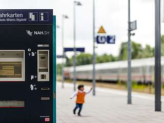 Links im Bild ist ein Farkartenautomat zu sehen und weiter hinten spielt ein Kind auf dem Bahnsteig.