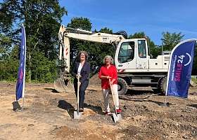 zwei Personen beim Spatenstich in Damp mit Bagger im Hintergrund