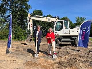 zwei Personen beim Spatenstich in Damp mit Bagger im Hintergrund