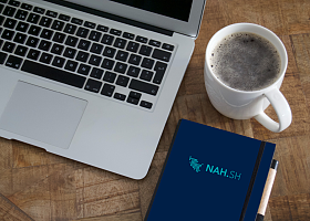 Laptop, Kaffeebecher und Notizbuch auf einem Schreibtisch