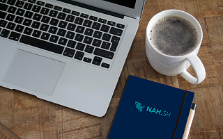 Laptop, Kaffeebecher und Notizbuch auf einem Schreibtisch