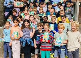 Viele Kinder stehen auf einer Treppe vor dem Schulgebäude und freuen sich über die Hausaufgabenhefte von NAH.SH