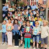 Viele Kinder stehen auf einer Treppe vor dem Schulgebäude und freuen sich über die Hausaufgabenhefte von NAH.SH