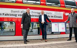 3 Herren stehen vor einem roten Zug