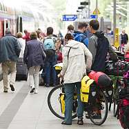 Fahrgäste mit Gepäck und Fahrrädern am Bahngleis