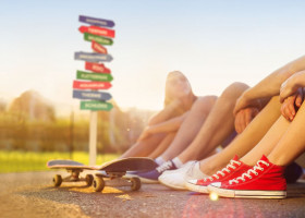 Beine von Jugendlichen mit Skateboard und  buntem Wegweiser im Hintergrund