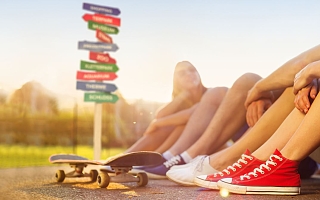 Beine von Jugendlichen mit Skateboard und  buntem Wegweiser im Hintergrund