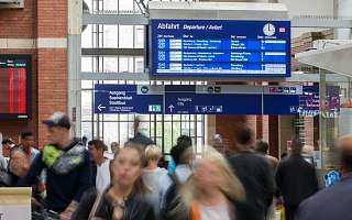 Symbolbild Bahnhof Pendler am Kieler Hbf mit einer Anzeigetafel im Hintergrund