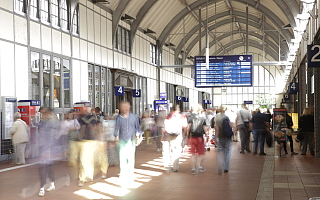 Pendler in Bahnhofshalle mit Anzeigetafel im Hintergrund 