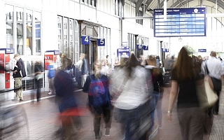 Pendler in Bahnhofshalle und Anzeigetafel im Hintergrund