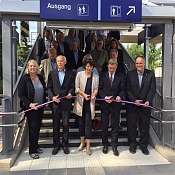 Gruppe von Personen bei einer Einweihung, schneidet ein Band vor einer Bahnhofstreppe durch