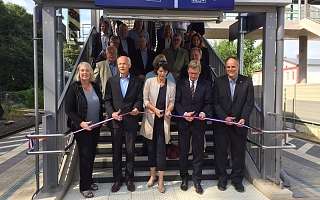 Gruppe von Personen bei einer Einweihung, schneidet ein Band vor einer Bahnhofstreppe durch