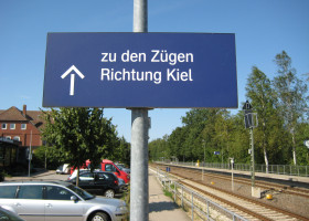 Parkplatz neben Bahngleisen mit dem Schild Züge in Richtung Kiel