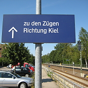 Parkplatz neben Bahngleisen mit dem Schild Züge in Richtung Kiel