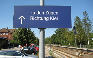 Parkplatz neben Bahngleisen mit dem Schild Züge in Richtung Kiel