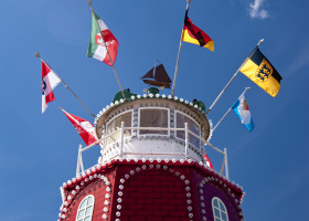 Leuchtturm in rot und weiß, oben mehrere Flaggen