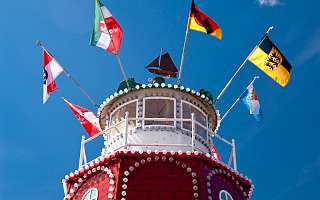 ThinkstockPhotos-545124016.jpg Leuchtturm in rot und weiß, oben mehrere Flaggen