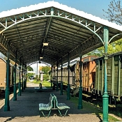 überdachter Bahnsteig mit alten Holzbänken und historischen Eisenbahnwagens auf beiden Seiten