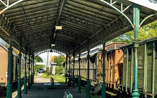 überdachter Bahnsteig mit alten Holzbänken und historischen Eisenbahnwagens auf beiden Seiten