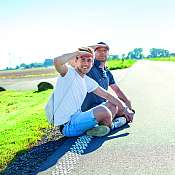 nahsh-soemmer2017-tash-teaser.jpg zwei Männer sitzen in der Sonne am Wegrand