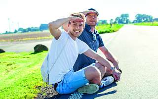 nahsh-soemmer2017-tash-teaser.jpg zwei Männer sitzen in der Sonne am Wegrand